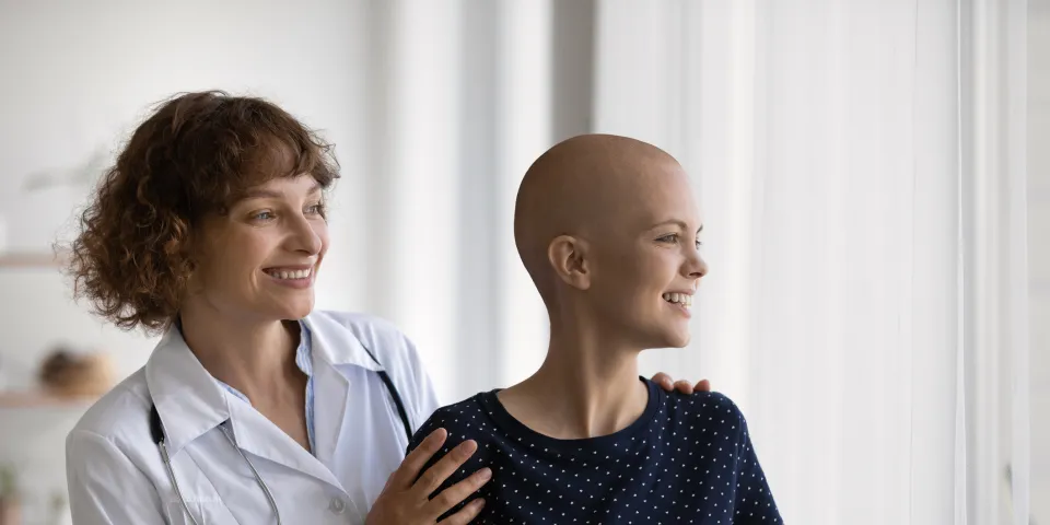 Smiling Caucasian doctor or nurse support comfort millennial woman struggle with oncology. Happy GP and optimistic female cancer patient look in distance dream of illness recovery or remission.