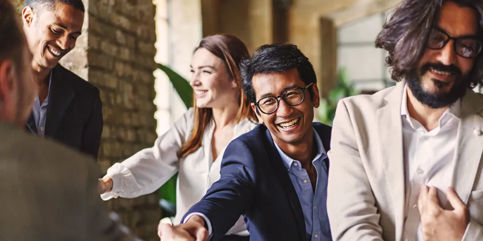 Group of diverse professionals celebrating with a handshake at a corporate event, embodying teamwork and achievement.