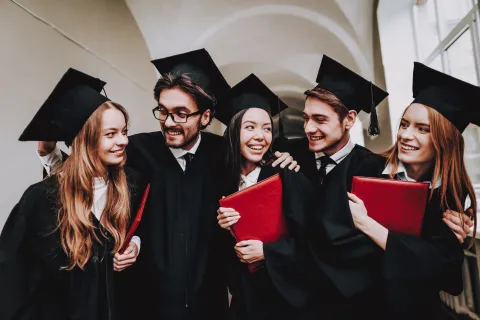 Five college graduates holding diplomas celebrating on graduation day