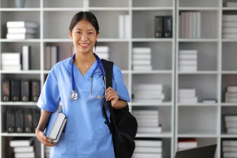 Nursing student smiling in library with bag over shoulder