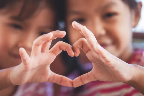 Two cute asian child girls making heart shape with hands together