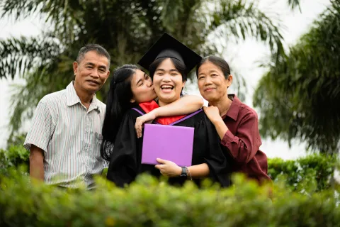 College graduate smiling and holding diploma while celebrating with family