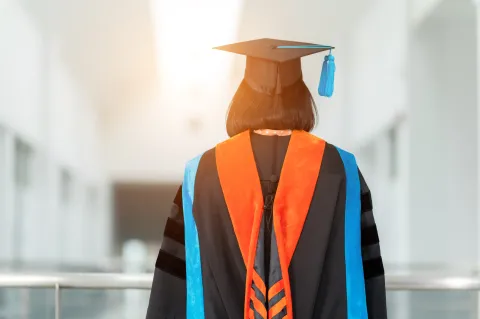 PhD student with their back facing viewer wearing an orange nursing hood