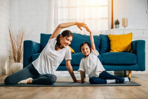 A mother coaches her little daughter in yoga creating a family bond filled with happiness relaxation and togetherness.