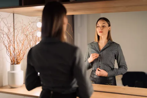 Self-confident woman looking at her reflection into the mirror indoors.